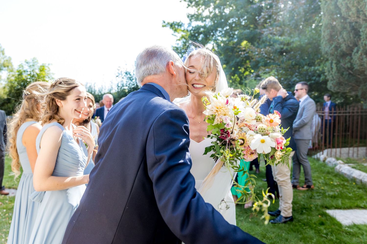 Wedding party celebrates on the church grounds with blue bridesmaid dresses and floral bouquets.
