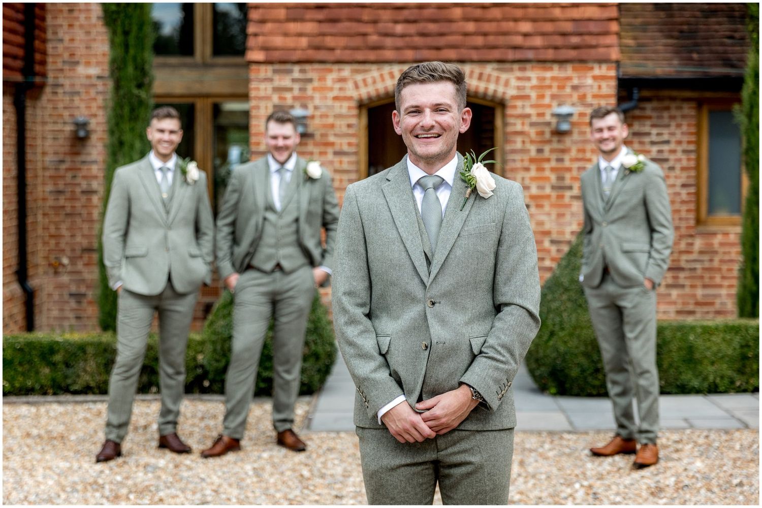 Groomsmen in light gray suits posing outside a brick building.
