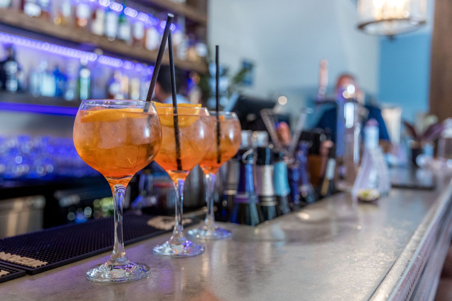 Cocktail glasses lined up on a modern bar counter with blue ambient lighting.