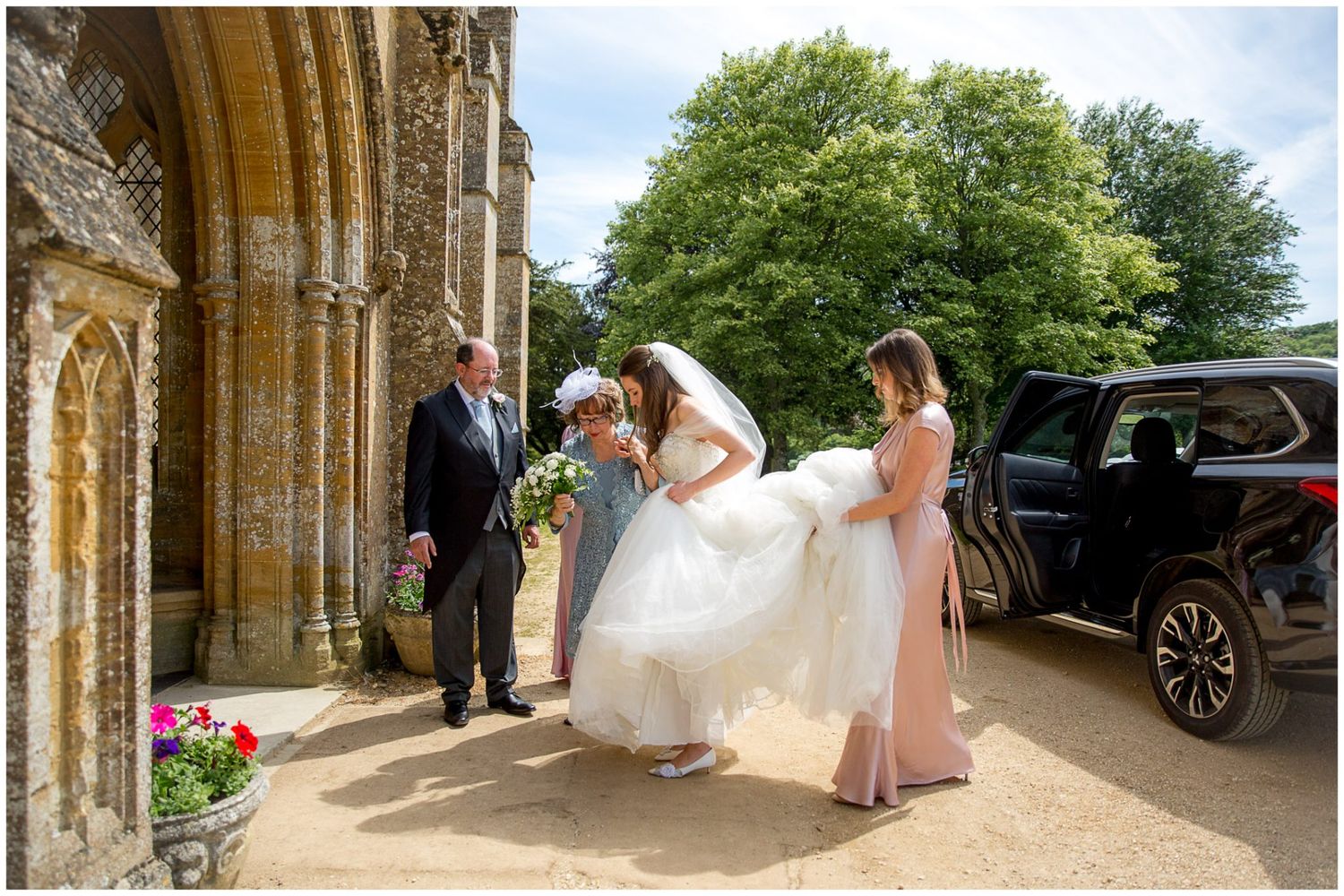 A wedding party gathers under a grand stone archway during an elegant outdoor ceremony.