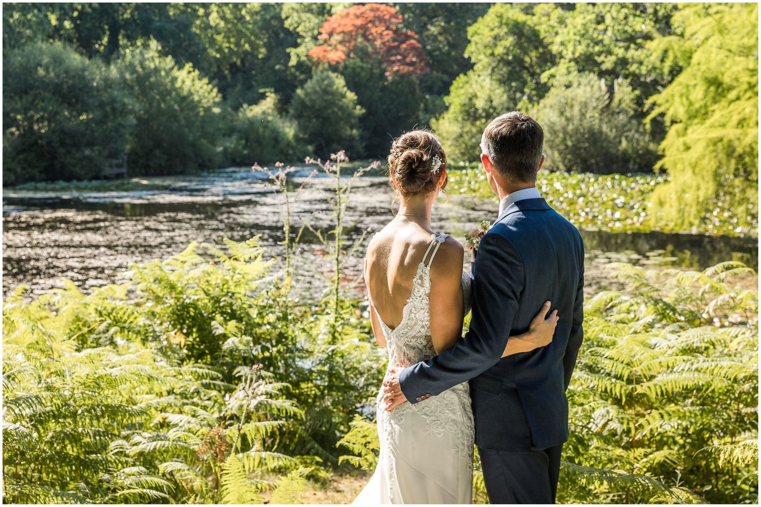 Bride and groom look out acros a lake at Walhampton School during their wedding photography portrait session