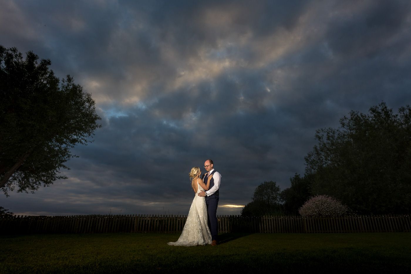 Dramatic sunset silhouettes of a wedding couple against moody evening sky.