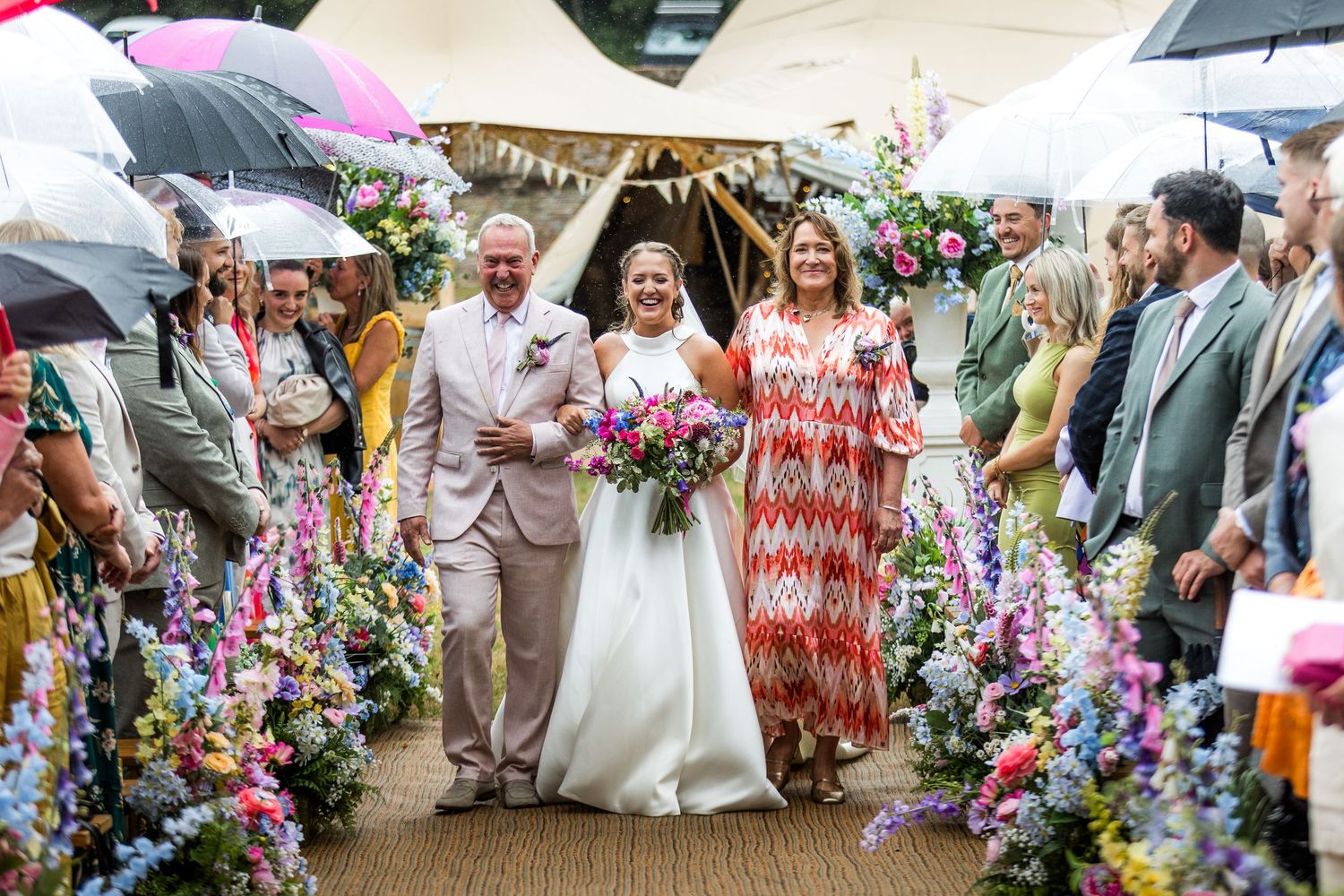 Wedding guests gathered around vibrant floral displays at an outdoor celebration.