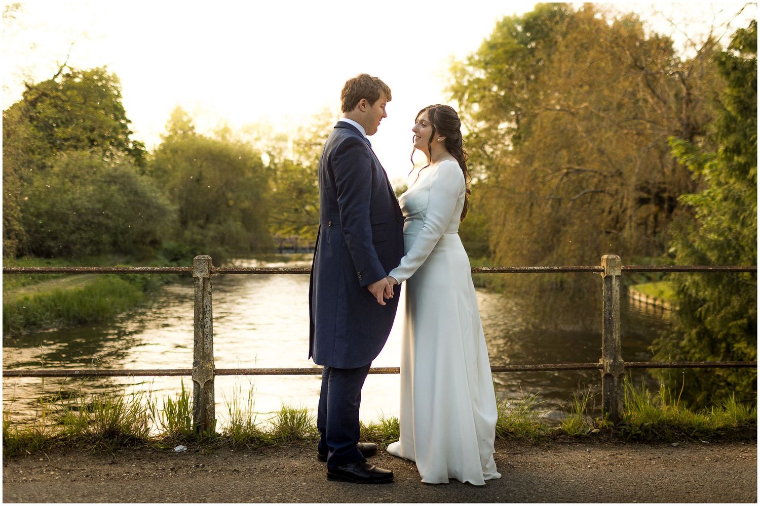 Couple in wedding attire standing by a scenic lake at golden hour.