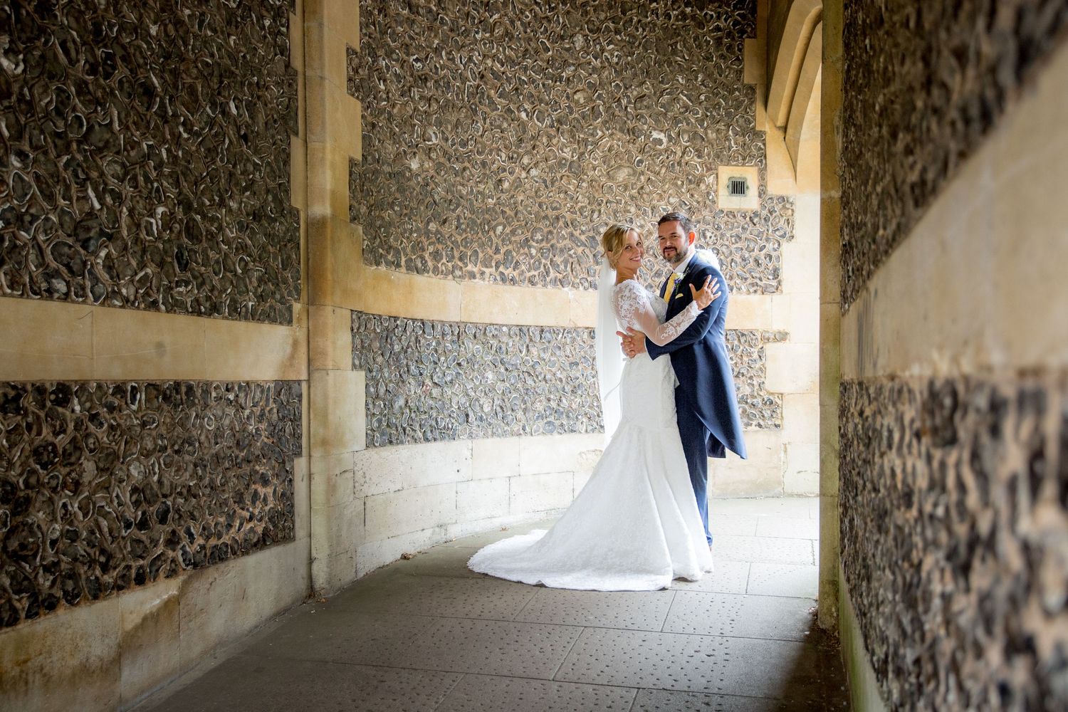 Artistic black and white wedding portraits in stone corridor with textured walls.