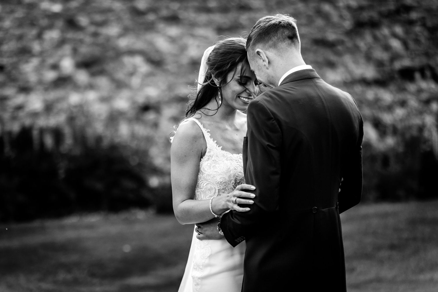 Romantic black and white wedding photography against stone wall backdrop.