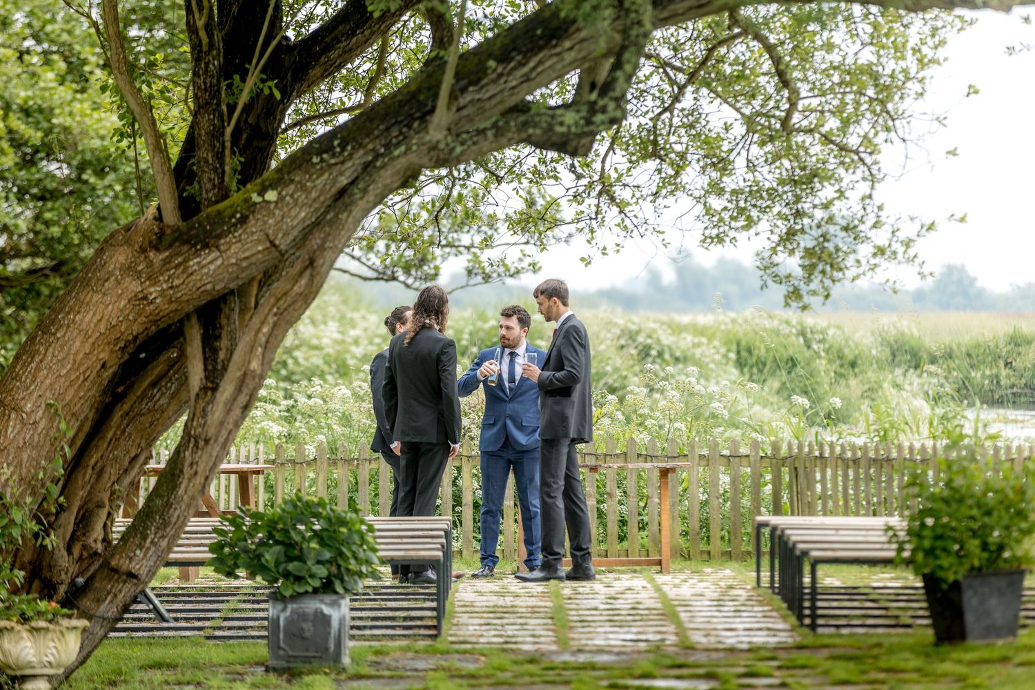 Scenic wedding venue with wooden fence and large tree creating natural archway.