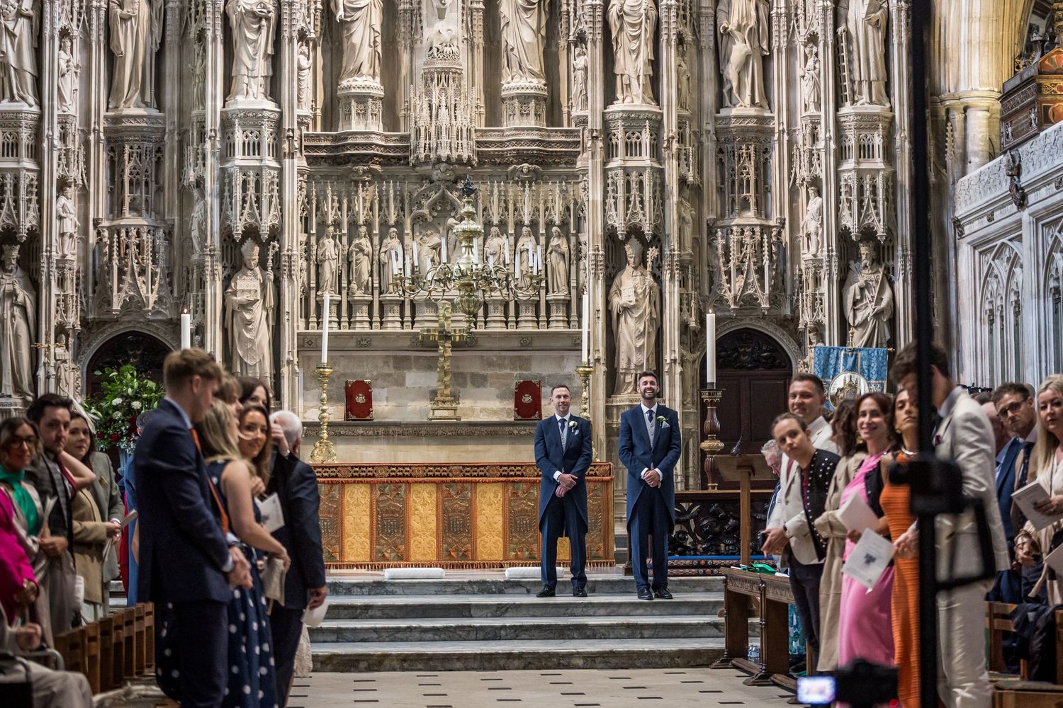 Wedding ceremony guests gather inside a majestic cathedral with ornate stone architecture.