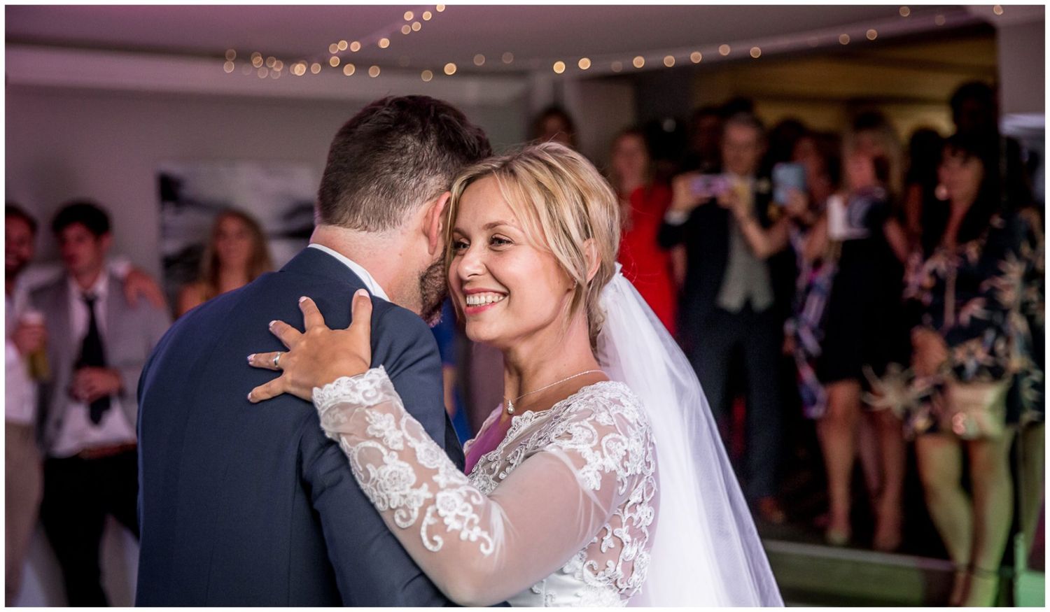 A romantic first dance sequence between newlyweds at an indoor wedding reception with soft lighting and guests watching.
