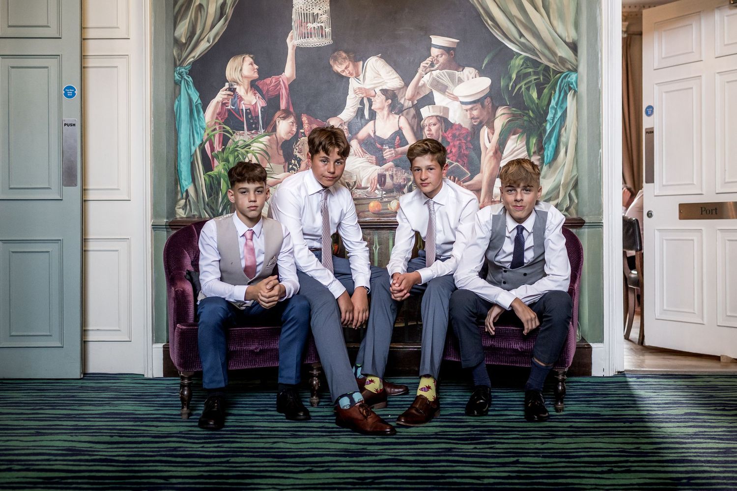 Groomsmen sitting casually against decorative wall during wedding celebration.