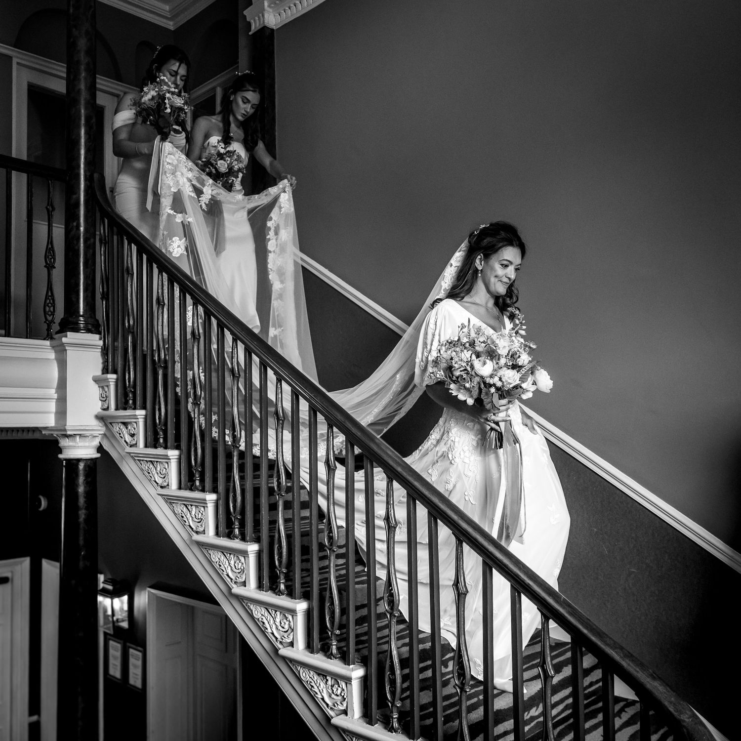 Black and white wedding photos showing elegant staircase moments with flowing white dress and bouquet.