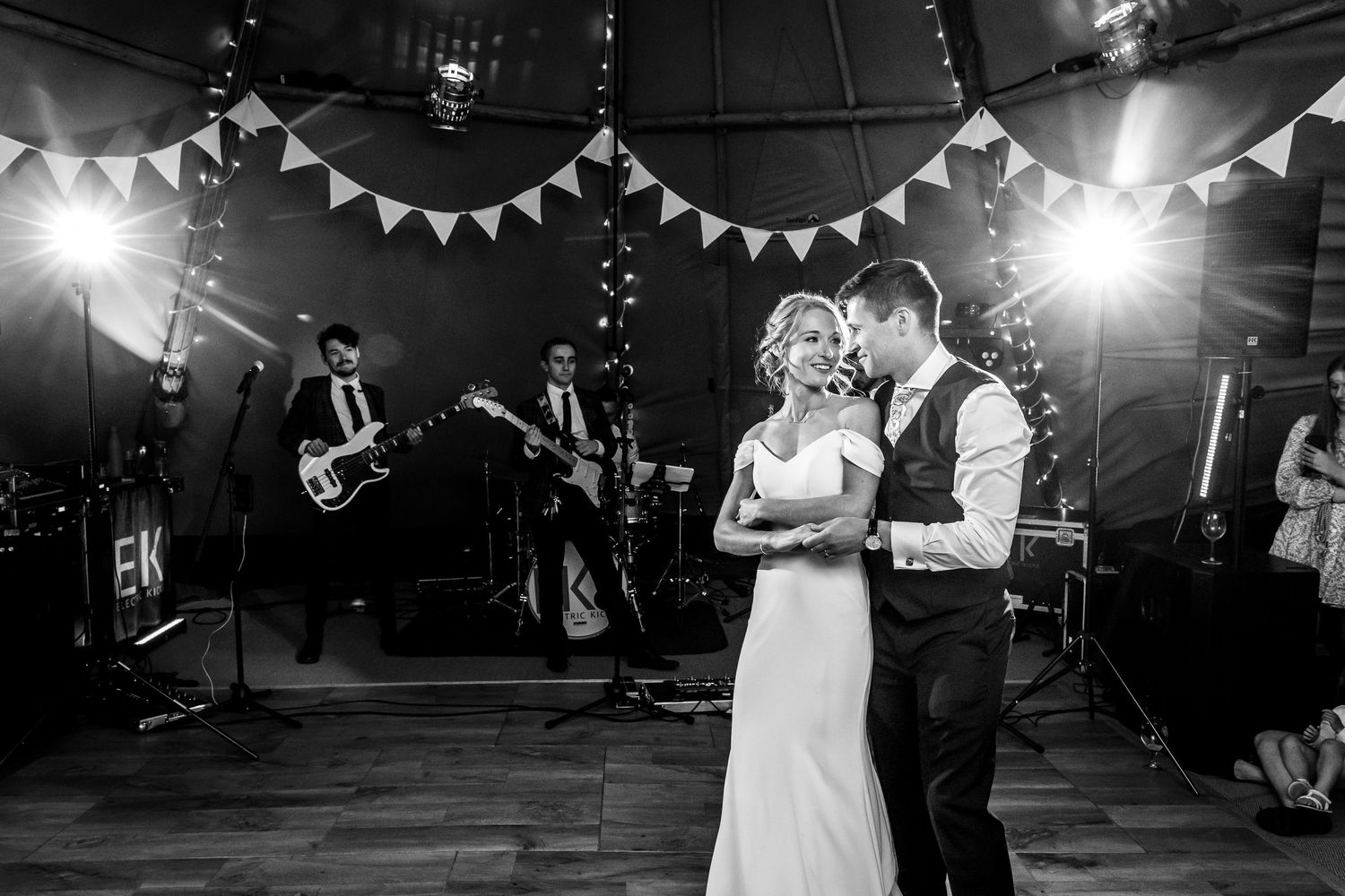 A couple shares their first dance under twinkling lights and bunting at their wedding reception.