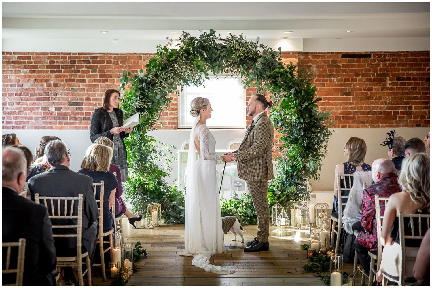 Wedding ceremony setup with floral arrangements and white chairs against brick walls.