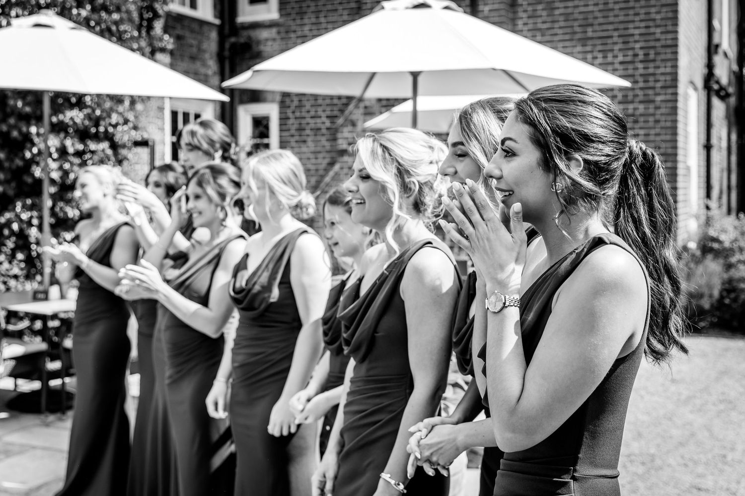 Wedding party reacts with joy outside under white umbrellas.