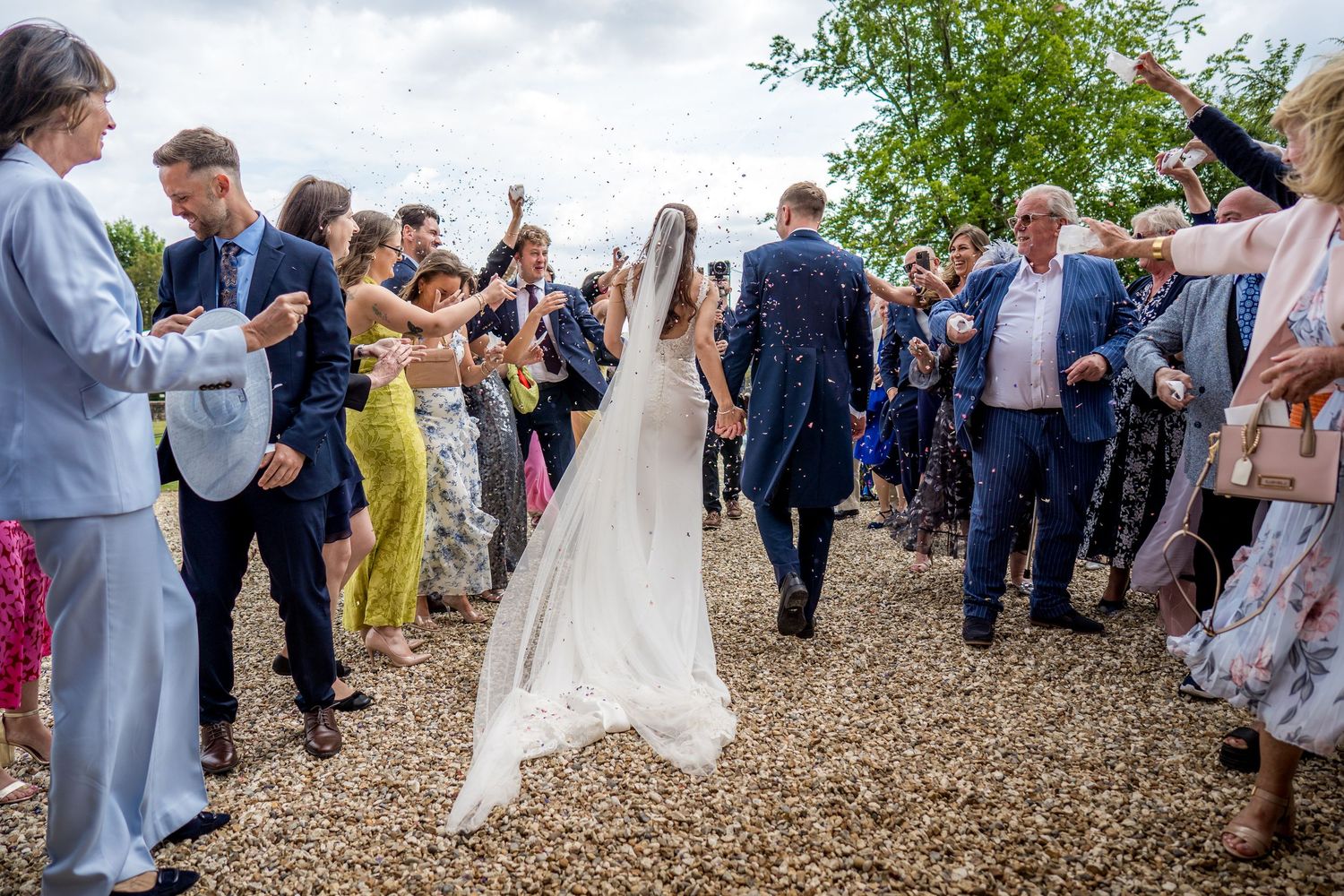 Wedding party and guests gather on a gravel path for outdoor celebrations.