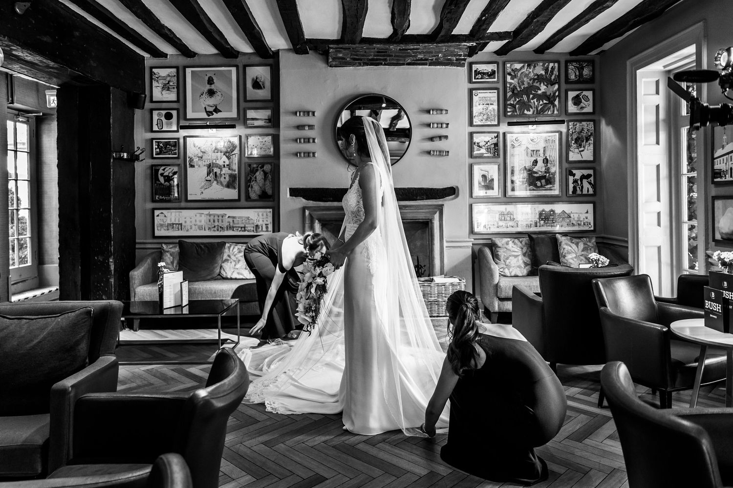 Black and white interior of a vintage bar with exposed beams and framed artwork on walls.