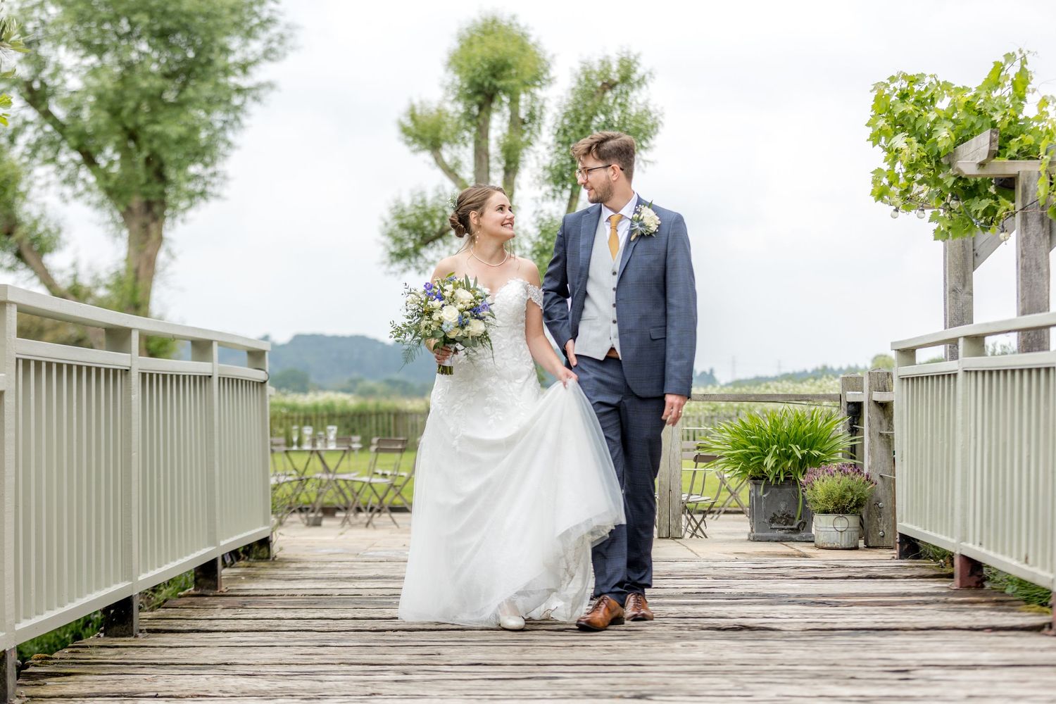Wedding couple poses on a white wooden boardwalk with greenery in the background.
