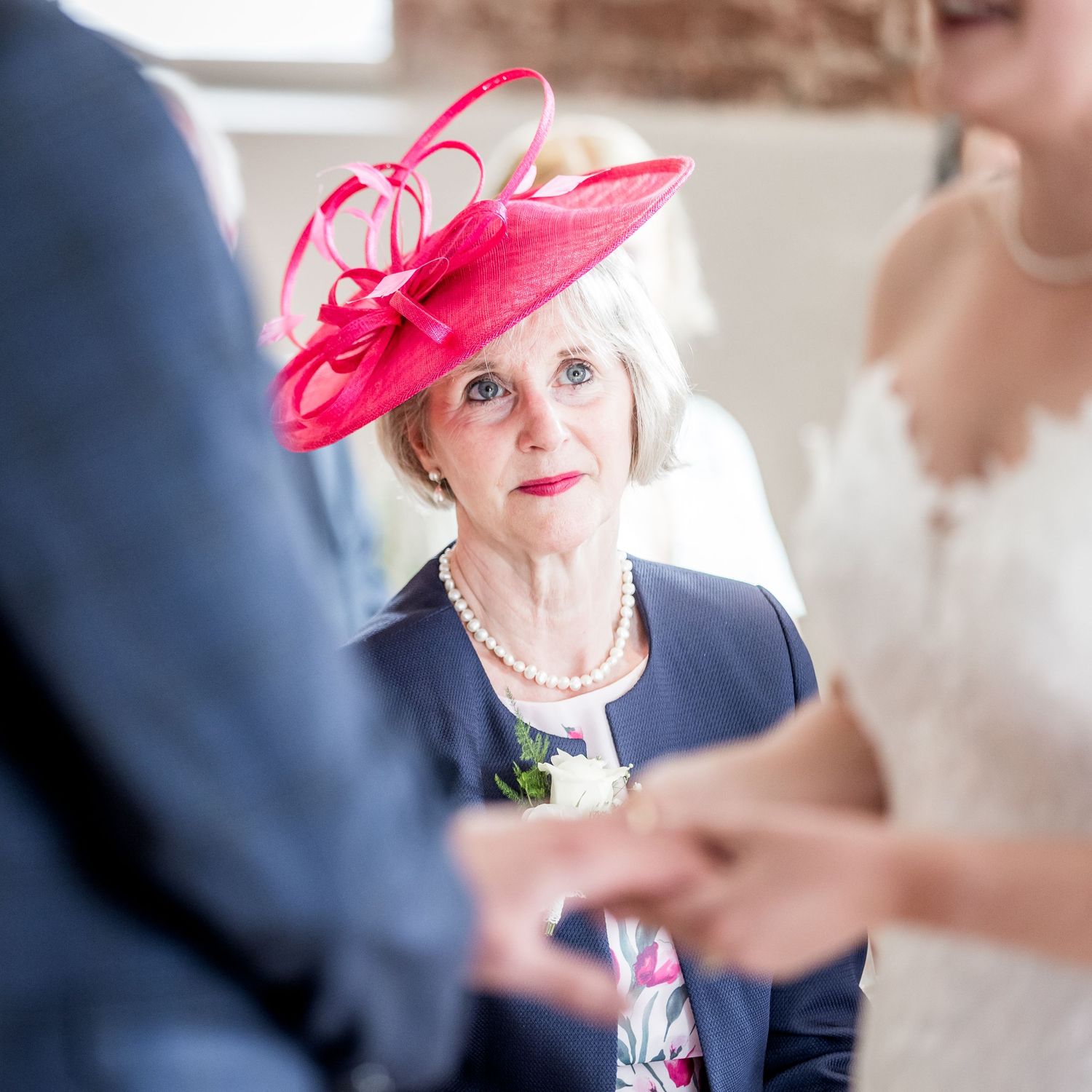 Wedding guests in formal attire gathered in sunlit brick interior space.