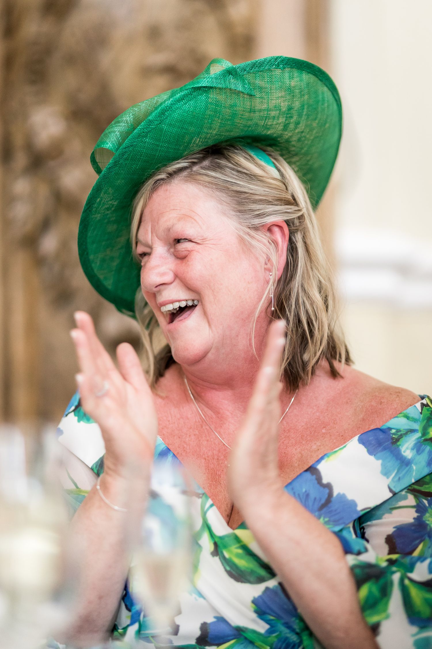 Guest in green hat and floral dress shows emotional reaction during wedding reception.