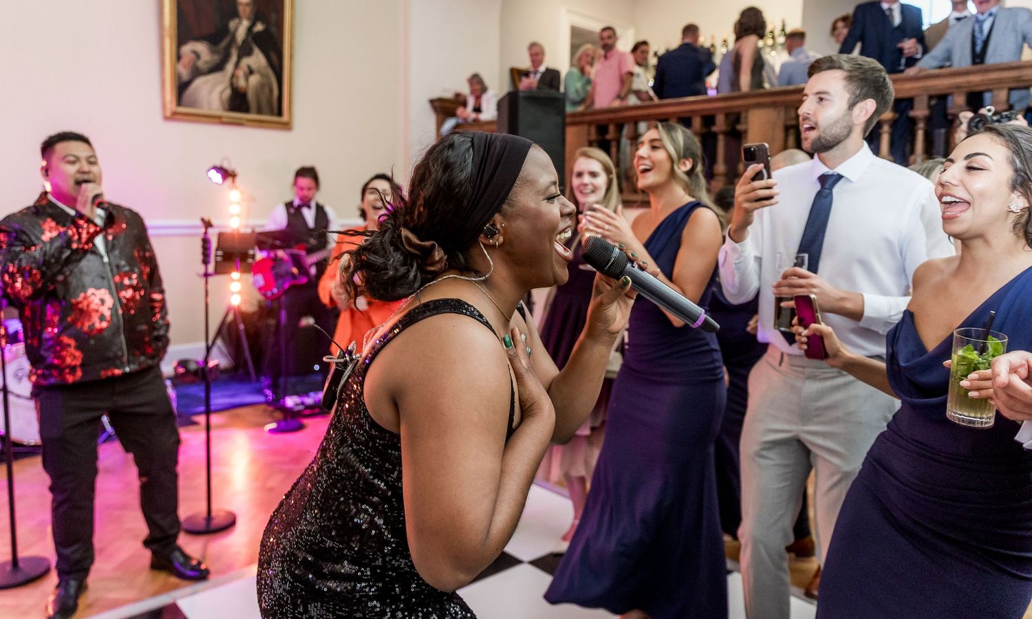 Wedding guests dance and celebrate together at an indoor reception venue with pink lighting accents.
