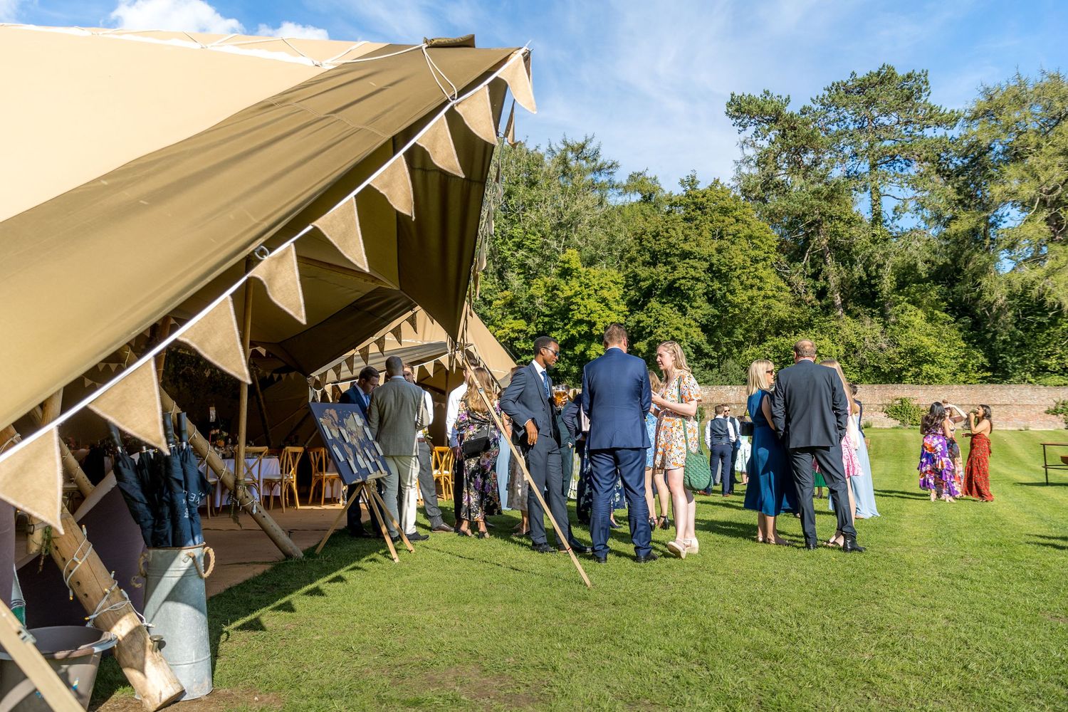 Outdoor wedding ceremony setup with tent and guests on grassy hillside.