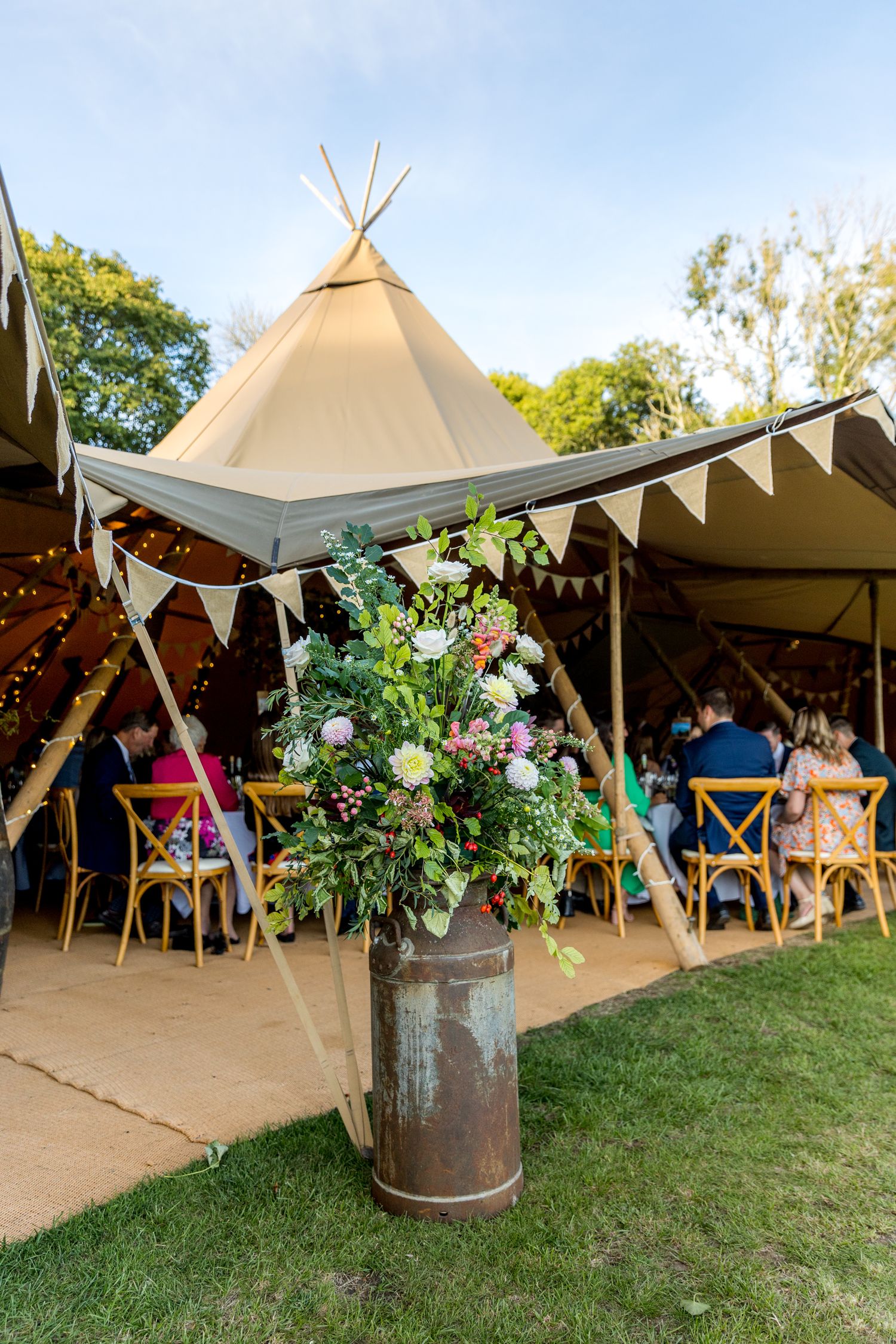 Elegant tipi tent decorated with floral arrangements and bunting for an outdoor celebration.