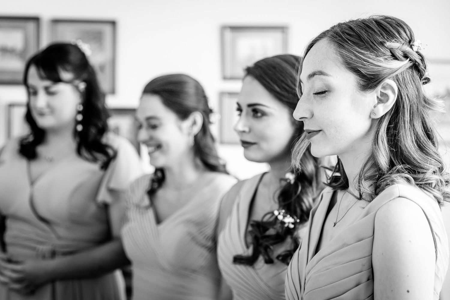 Four bridesmaids stand in a row during wedding preparations, captured in black and white.