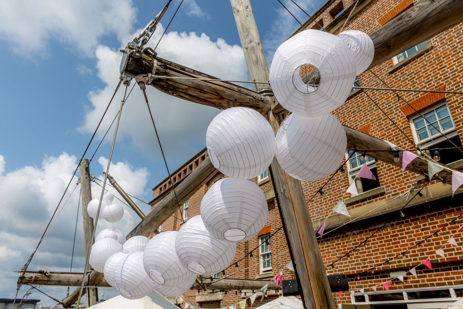 White paper lanterns hanging from wooden beams against a brick building facade.