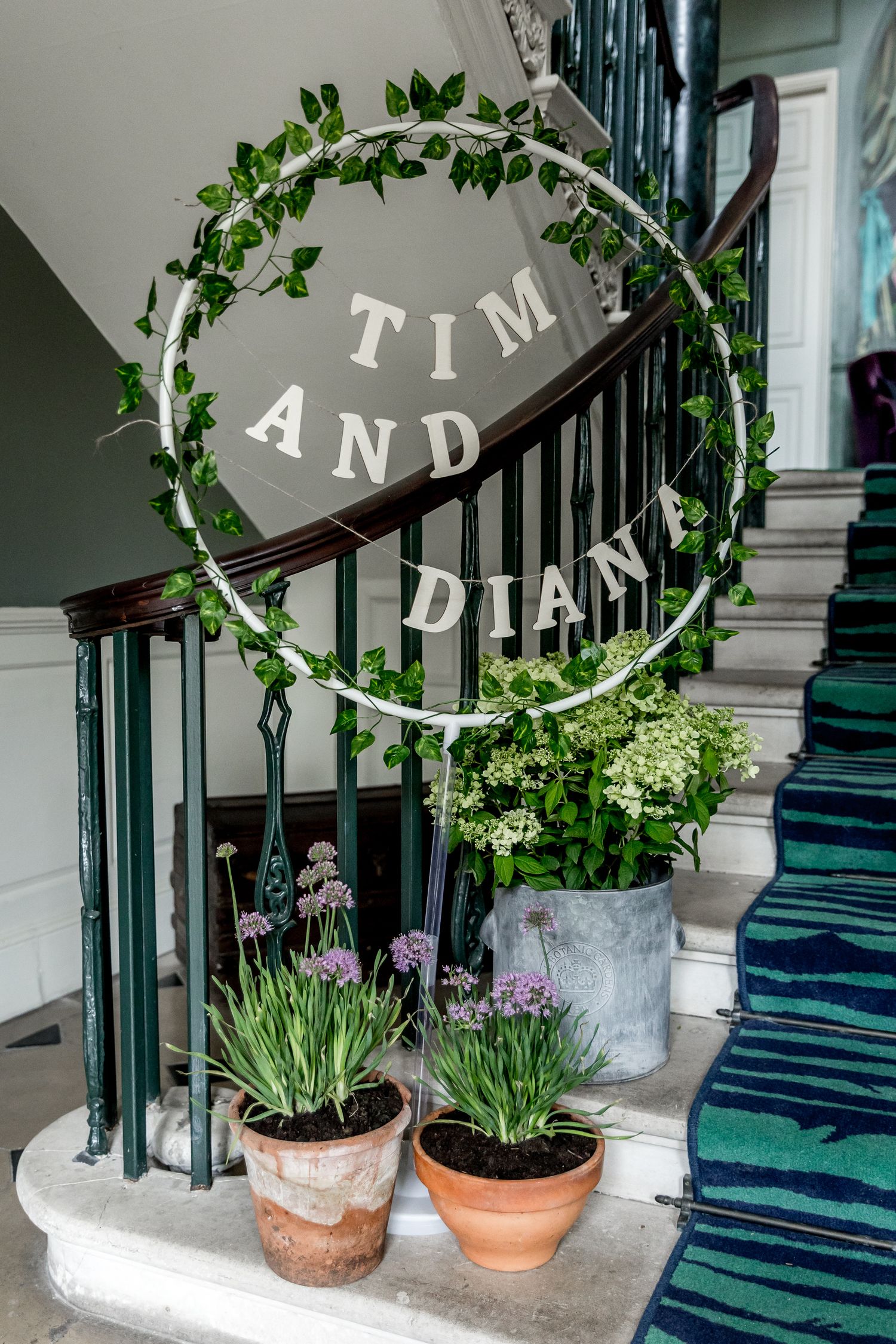 Decorative greenery and potted plants adorning a staircase with navy striped carpet runner.