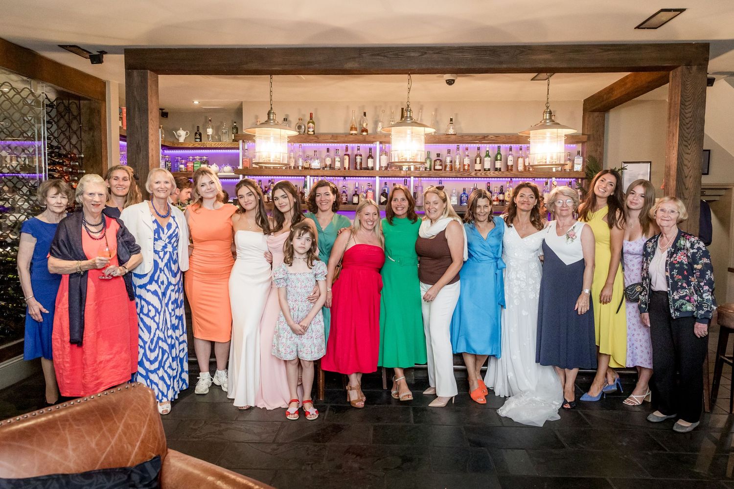 Large group photo of guests in colorful attire lined up against an indoor venue wall.