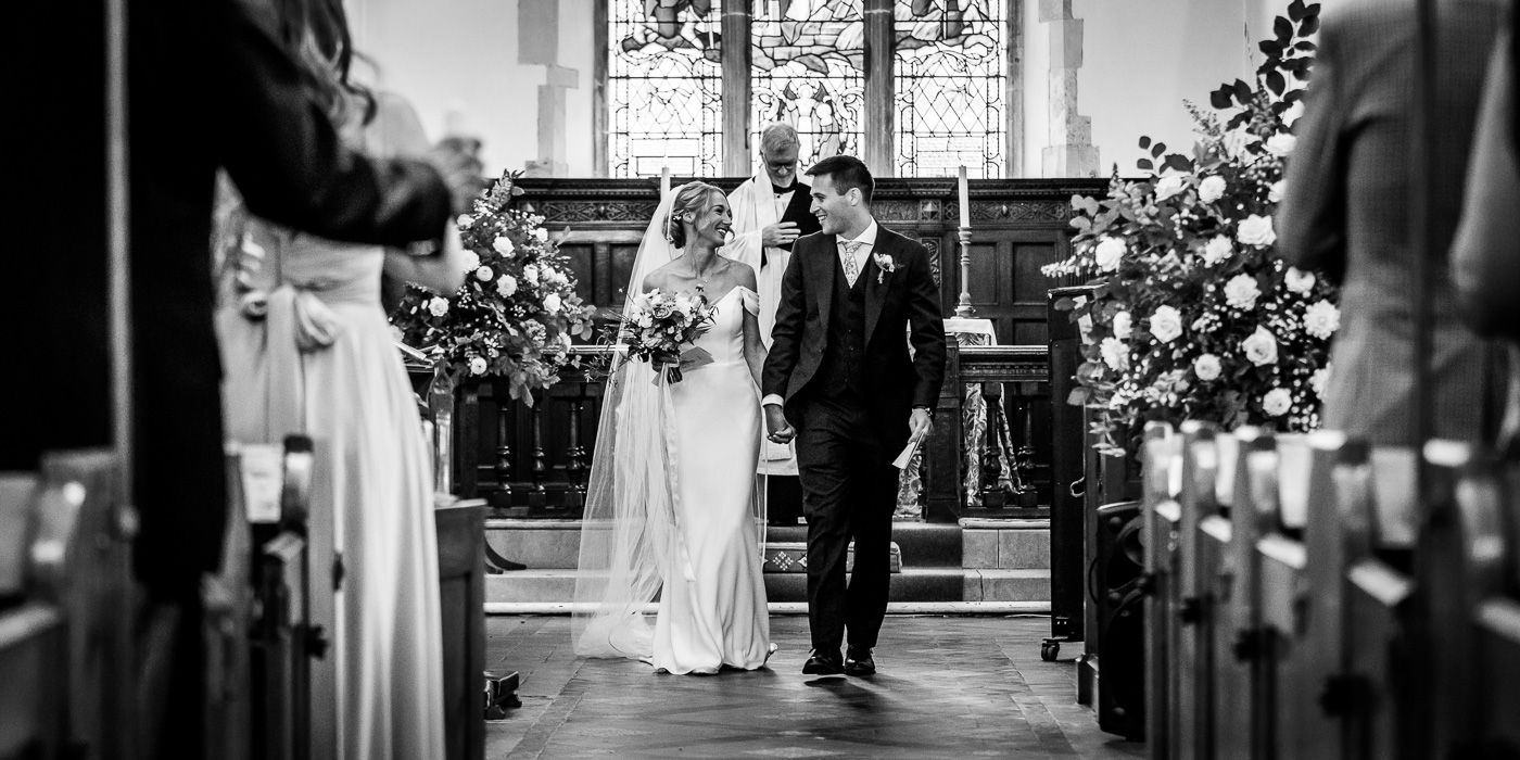 Black and white church aisle view during wedding ceremony with stained glass windows.