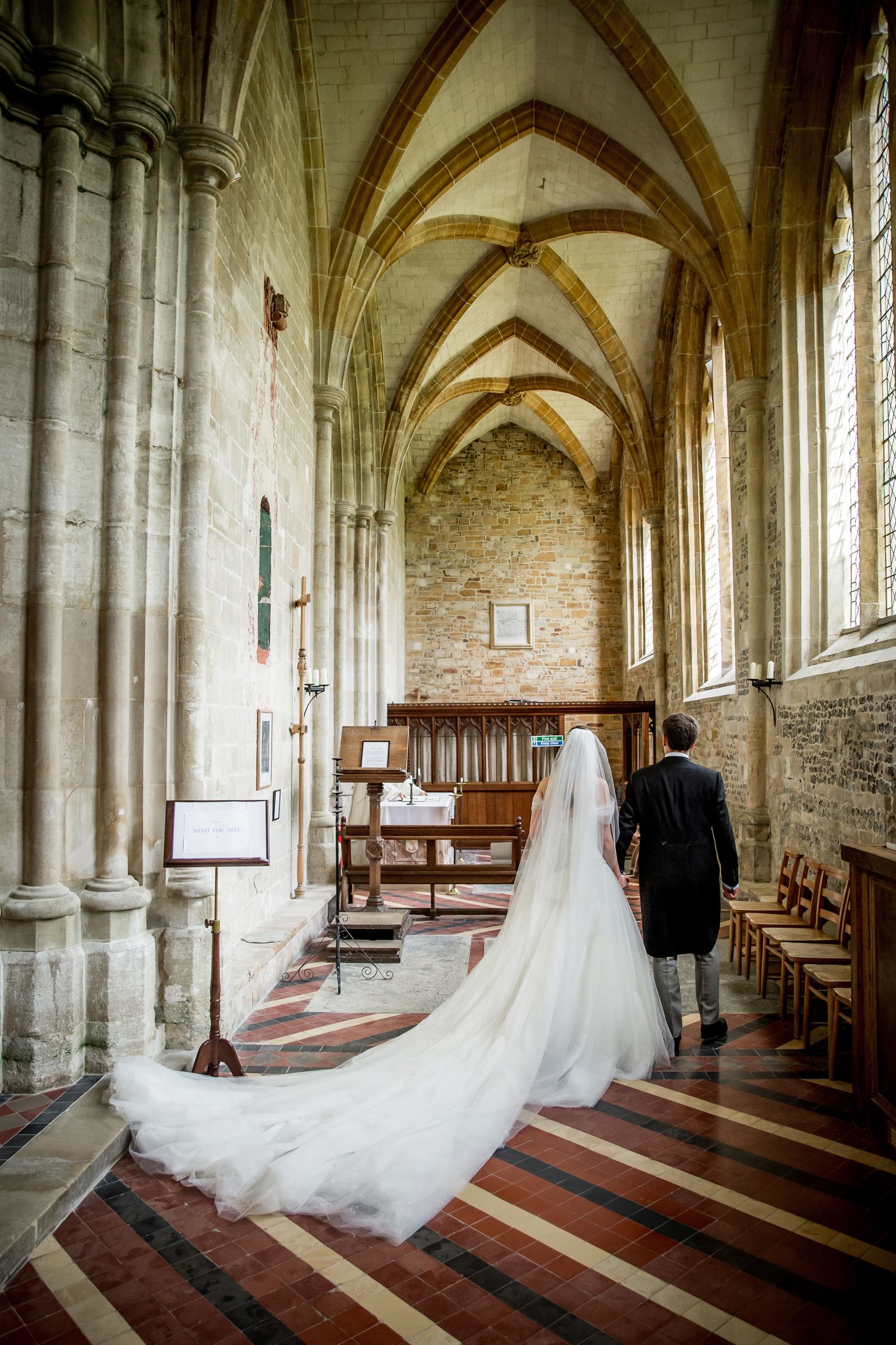 Wedding couple walking through gothic church cloisters with vaulted ceilings and stone columns.
