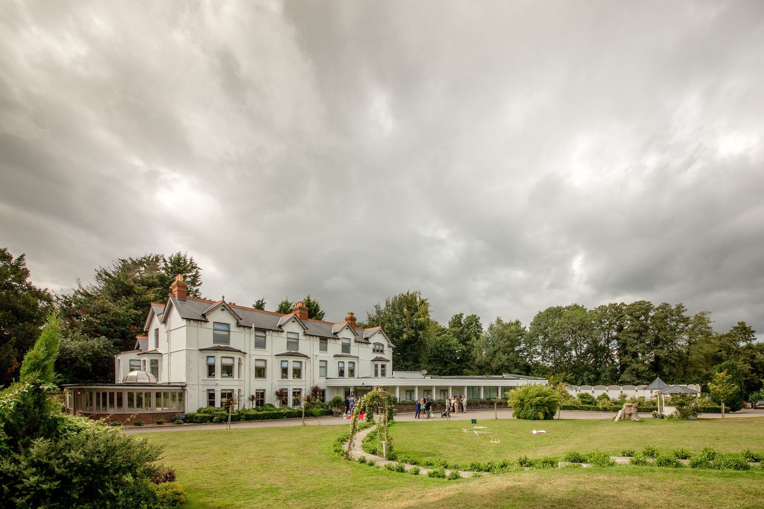 Sweeping panoramic view of an elegant white country estate with manicured grounds under cloudy skies.