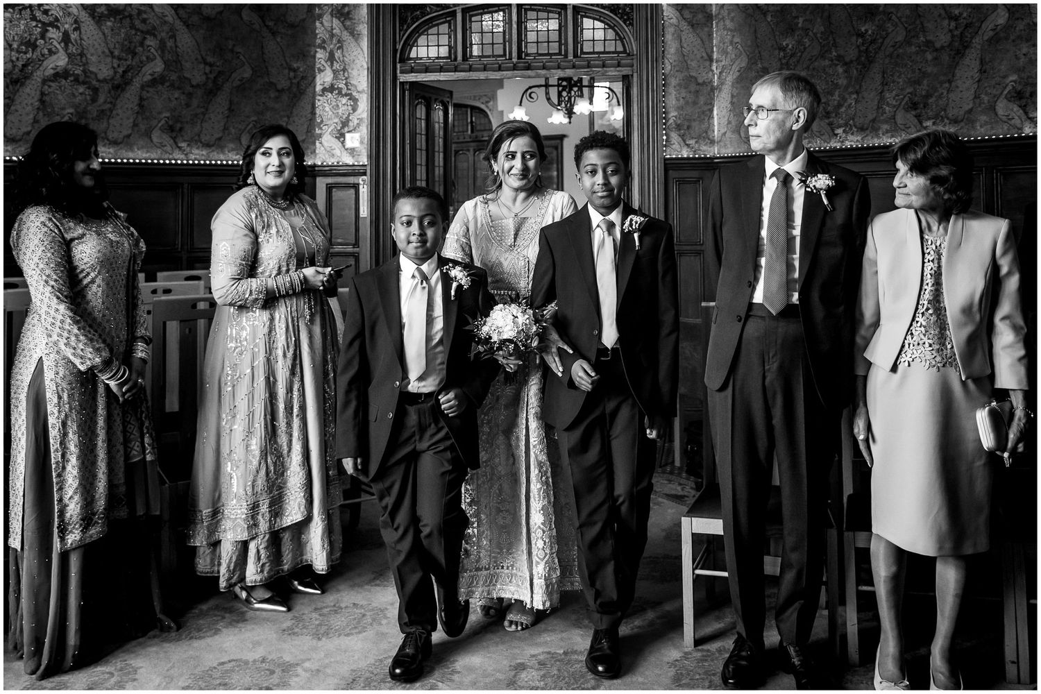 Wedding party and guests socializing in a grand room with vintage decor.