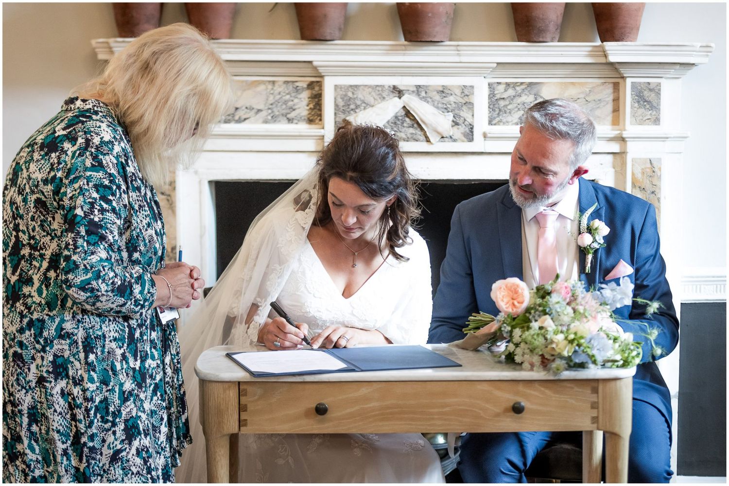 People signing documents at a wooden table during a formal ceremony.