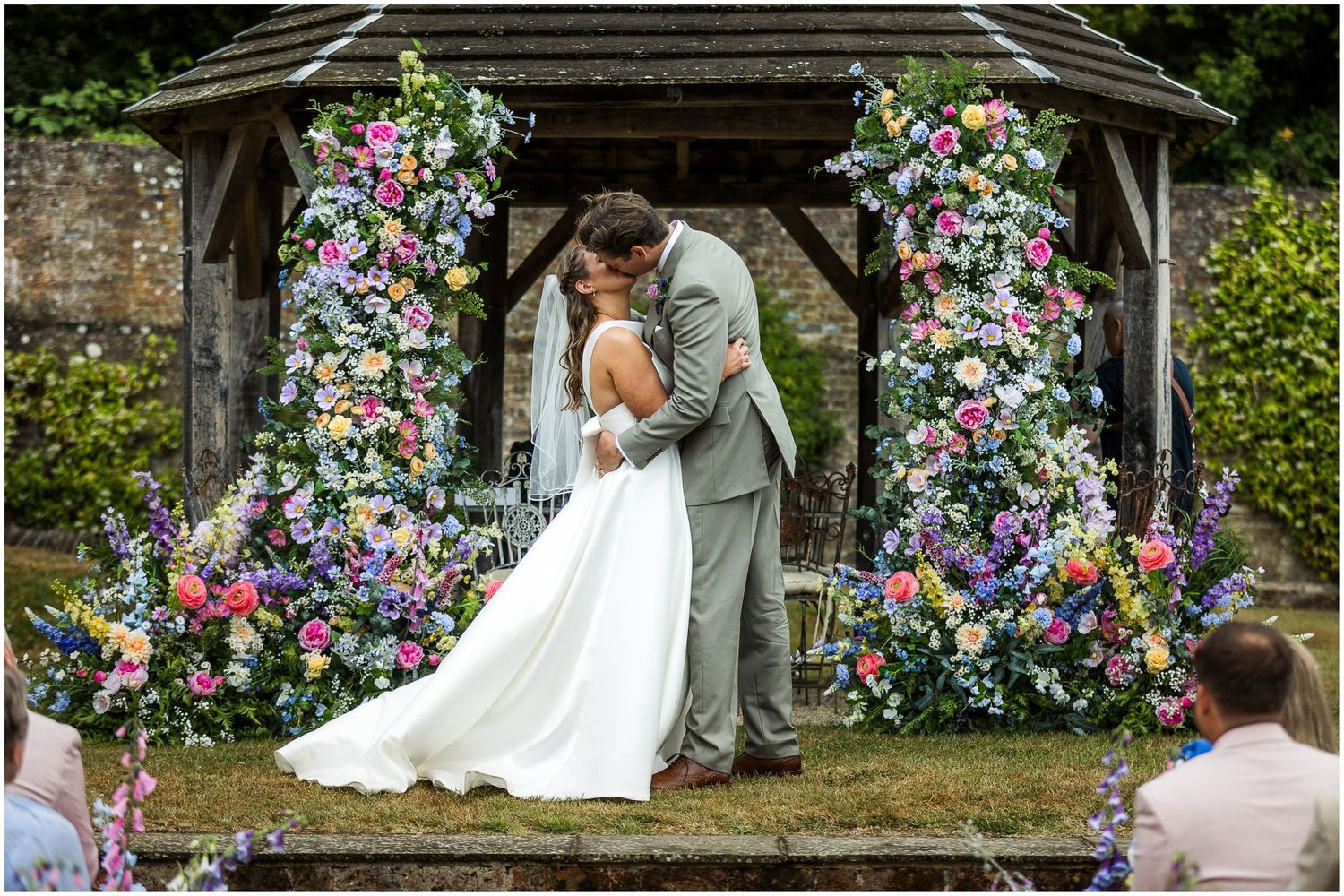 Bride and groom share first kiss under floral arch at outdoor wedding ceremony at the Holywell Estate