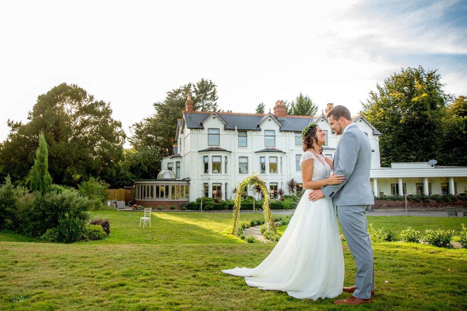 Bride and groom posed for a wedding photograph in the gardens of Southdowns Manor with the venue behind them