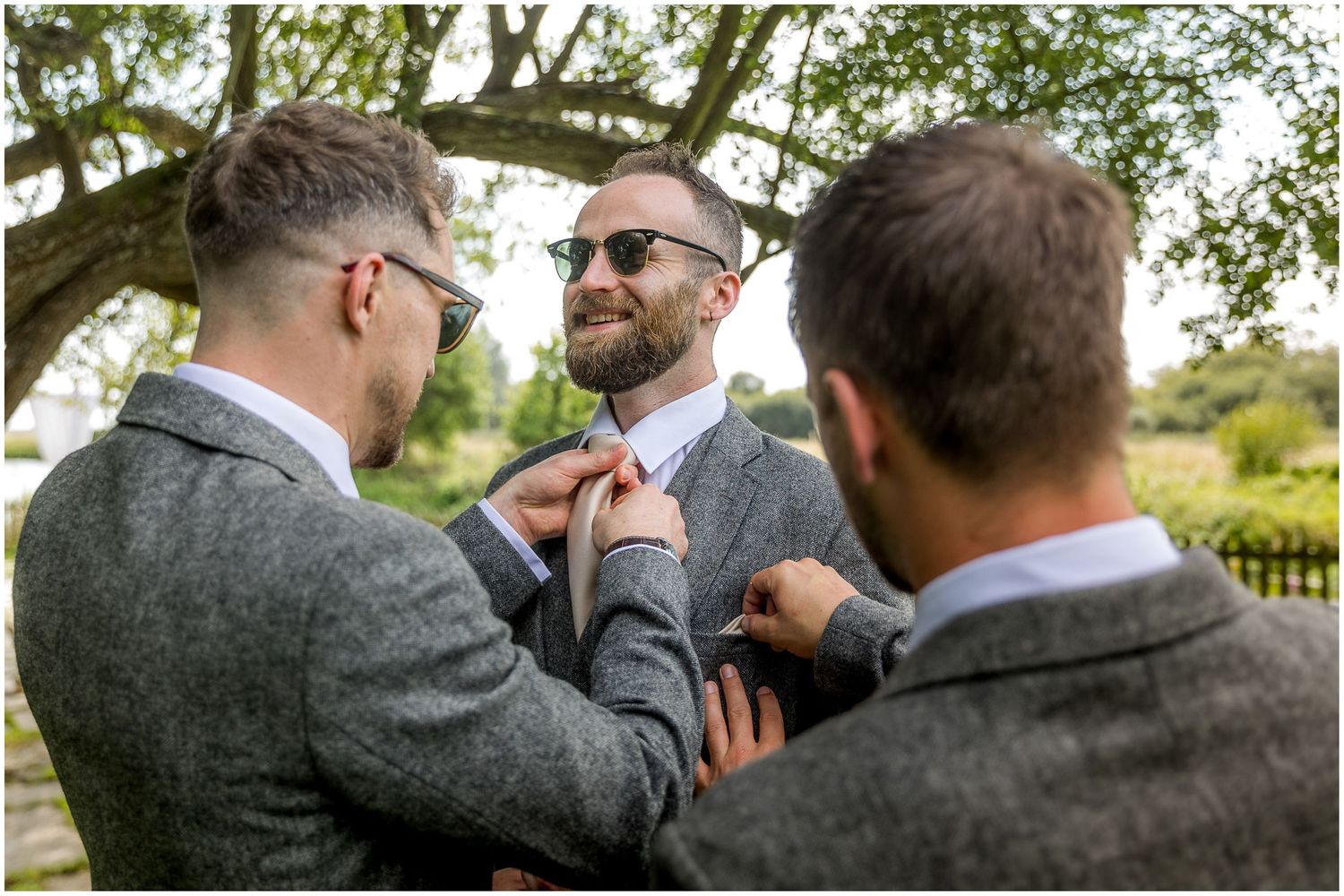 Groomsmen helping adjust tie and formal attire before wedding ceremony.