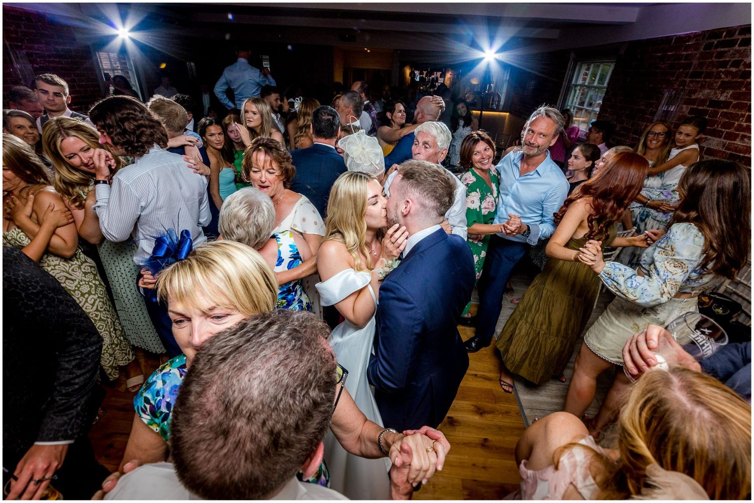 Panoramic view of a wedding reception dance floor with bright lighting and dancing guests.