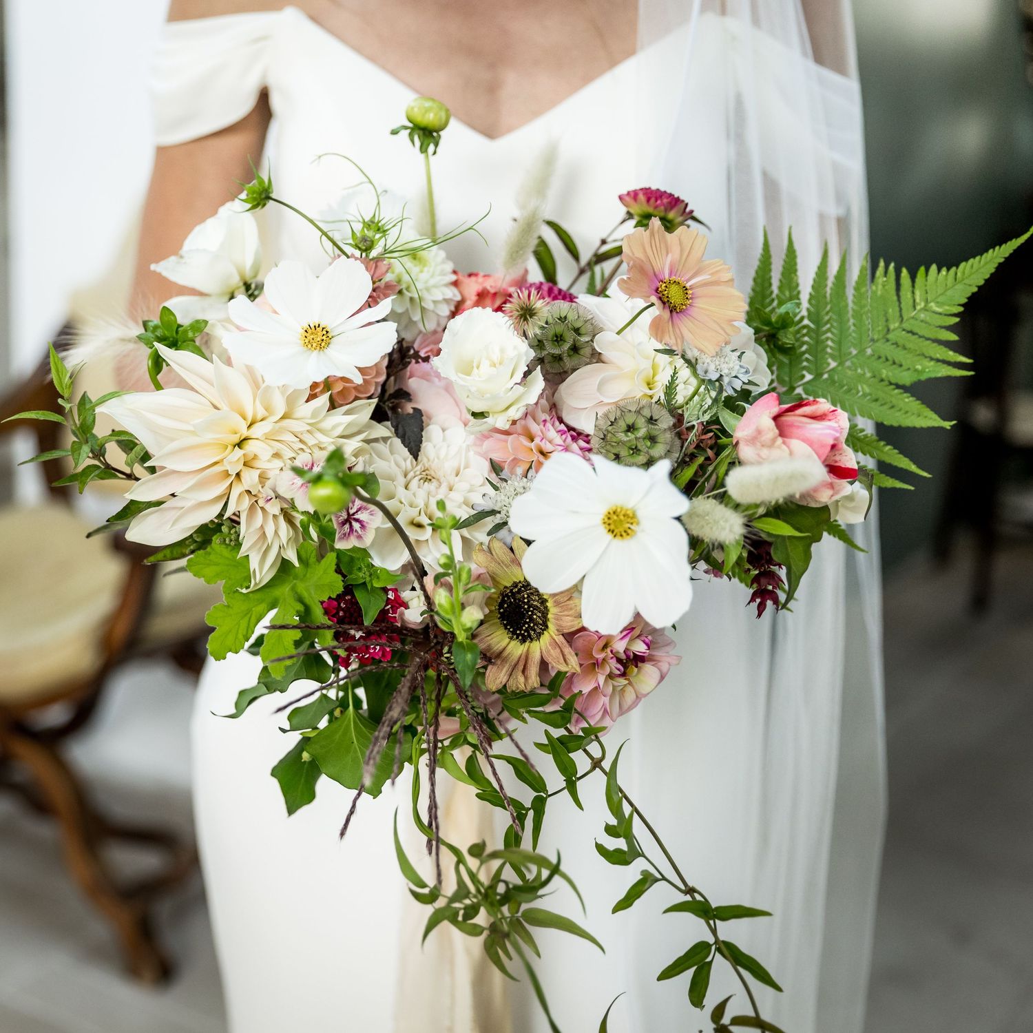 A romantic bridal bouquet featuring white dahlias, cosmos, and trailing greenery.