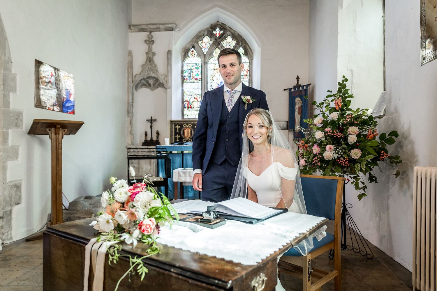 Church interior with stone archways and stained glass windows decorated for a wedding ceremony.