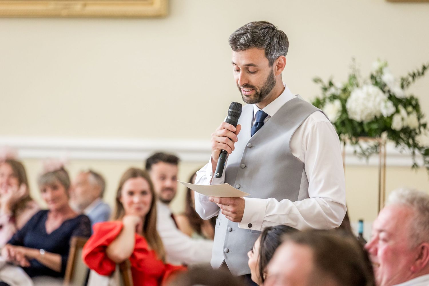 Wedding reception speeches being delivered at an elegant indoor venue with white decor.