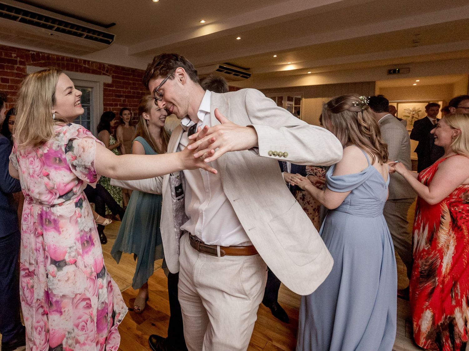 Guests dancing in pairs at a wedding reception with brick walls and ambient lighting.