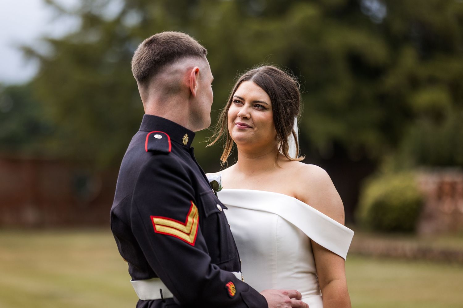 A couple in wedding attire embraces outdoors during their wedding photoshoot in a garden setting.