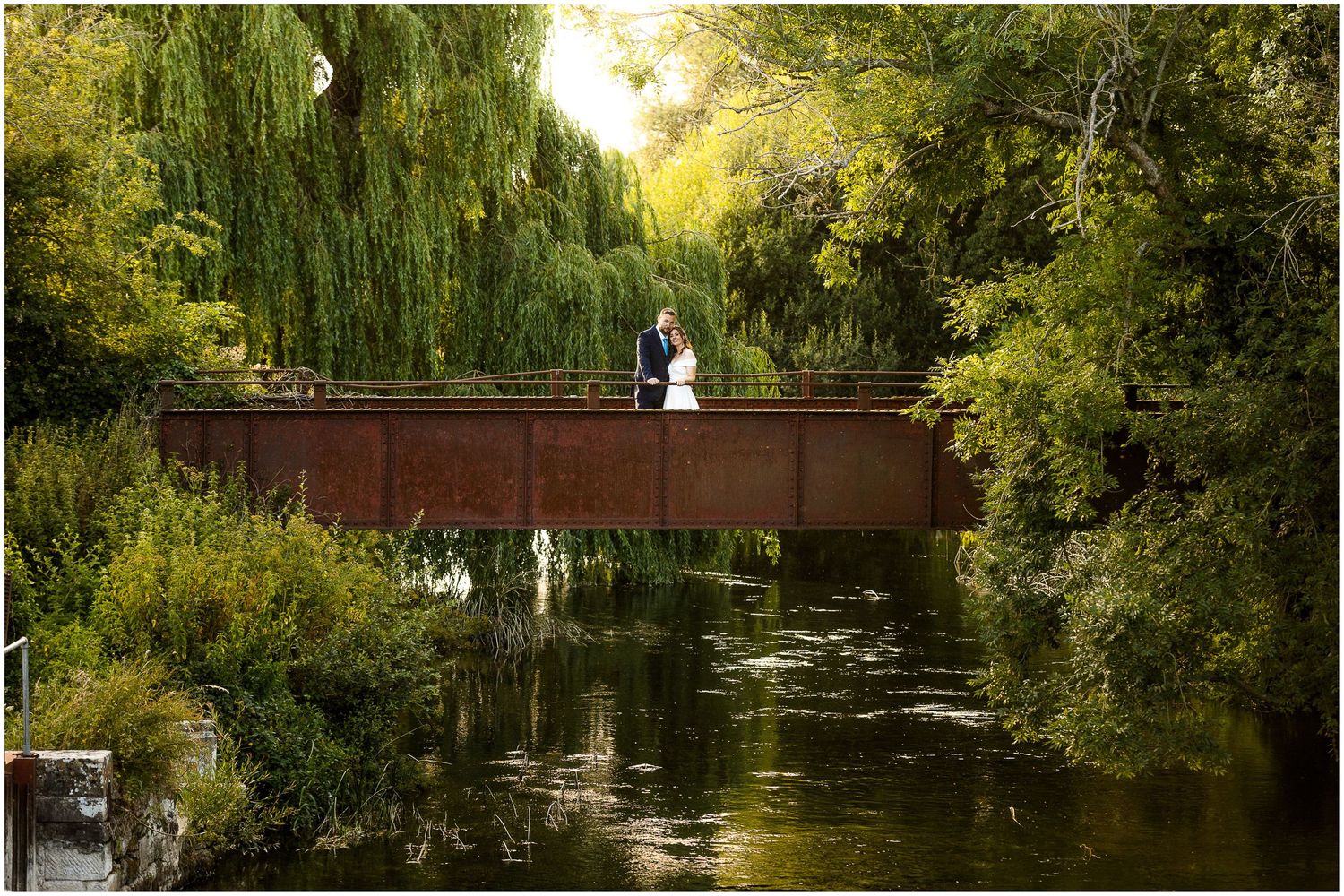 Classic wide wedding portrait photograph of bride and groom by the river behind Sopley Mill