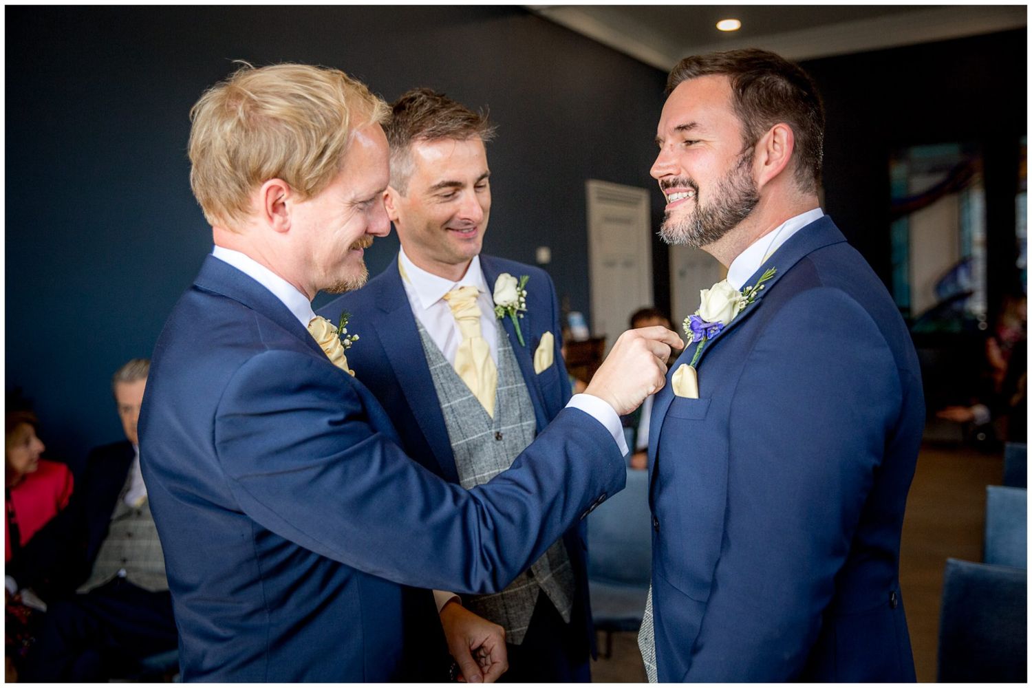Groomsmen in navy blue suits share a candid moment of laughter during a wedding celebration.