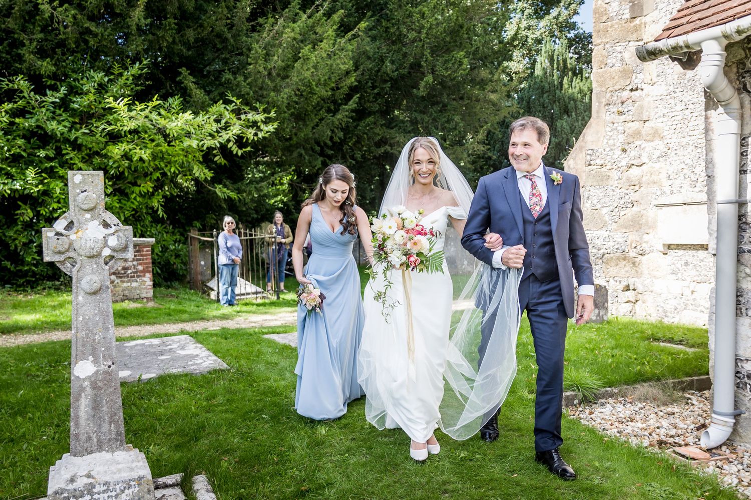 Wedding party poses among gravestones in historic church cemetery.