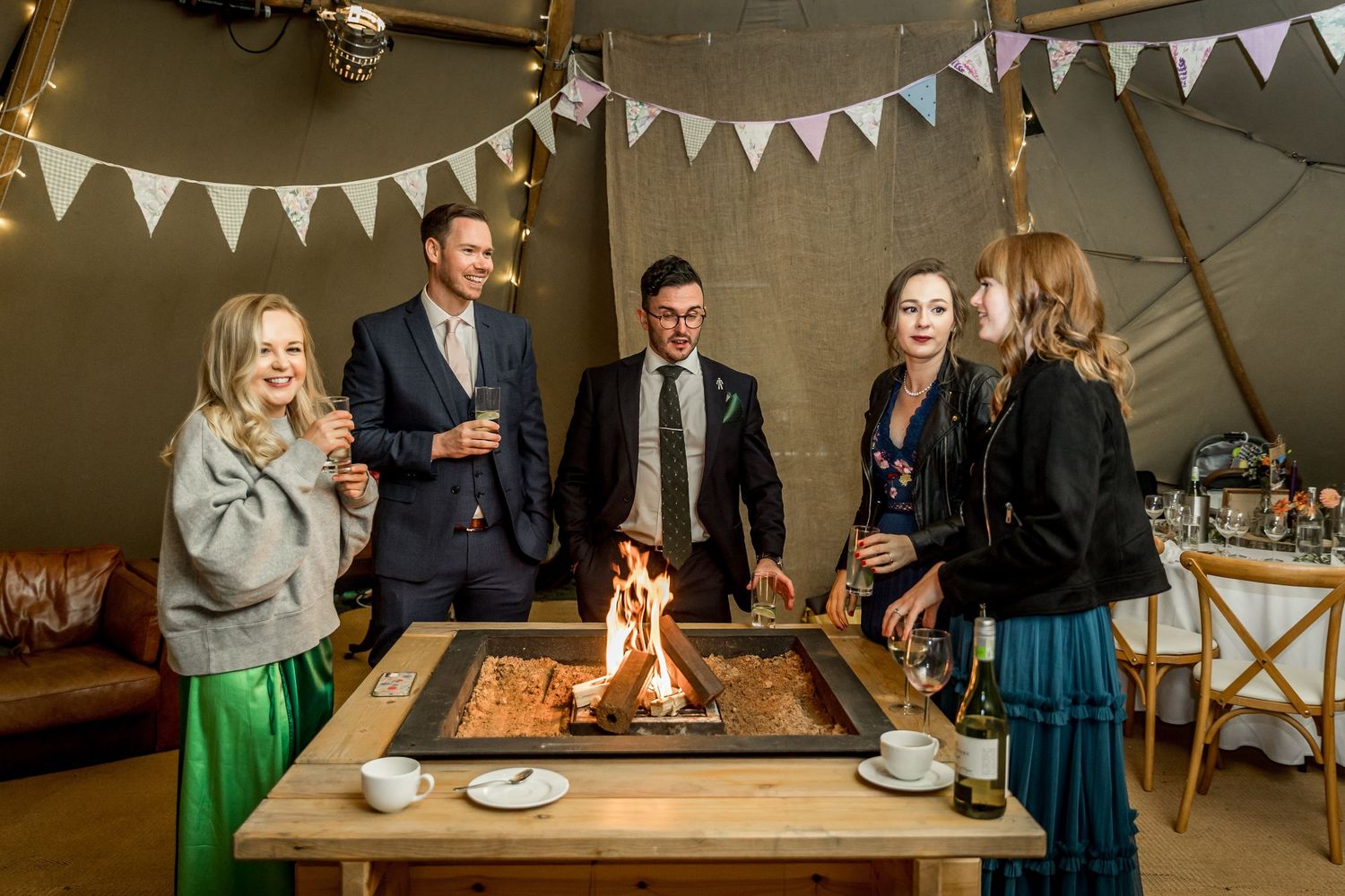 Wedding reception inside a tipi tent with bunting decorations and a fire pit.