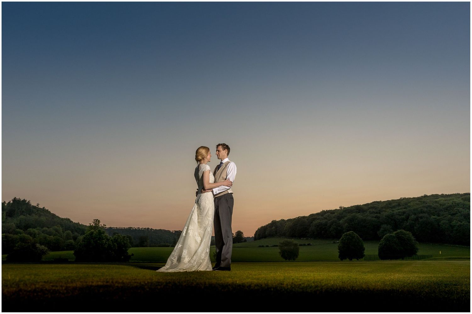 Elegant couple posing in meadow against dramatic sunset sky.