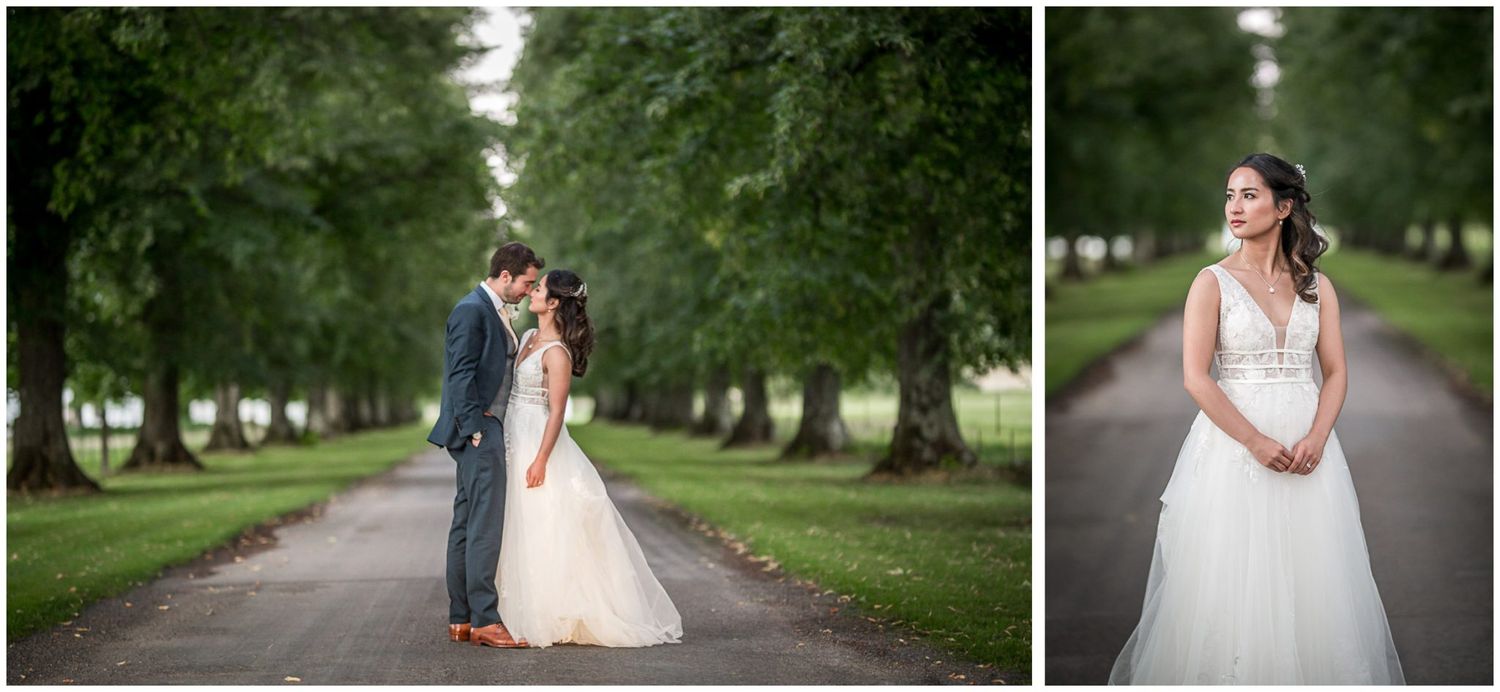 Romantic wedding couple embraces on a tree-lined path in an elegant outdoor setting.